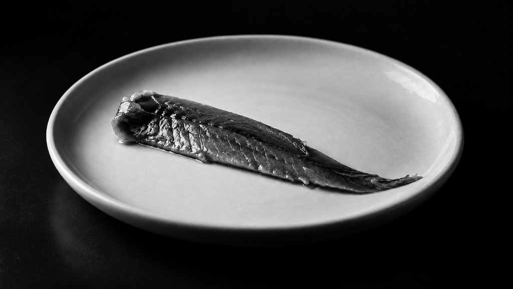 Ein Anchoa-Filet auf einem hellen Teller vor schwarzem Grund.